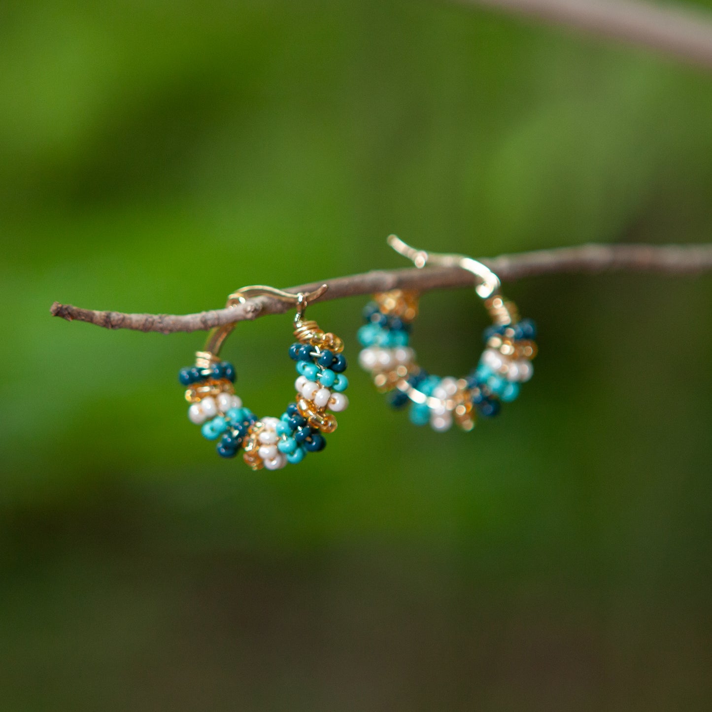 Handmade mini hoop earrings embellished with colorful beads and featuring bronze stud accents and gold plating.