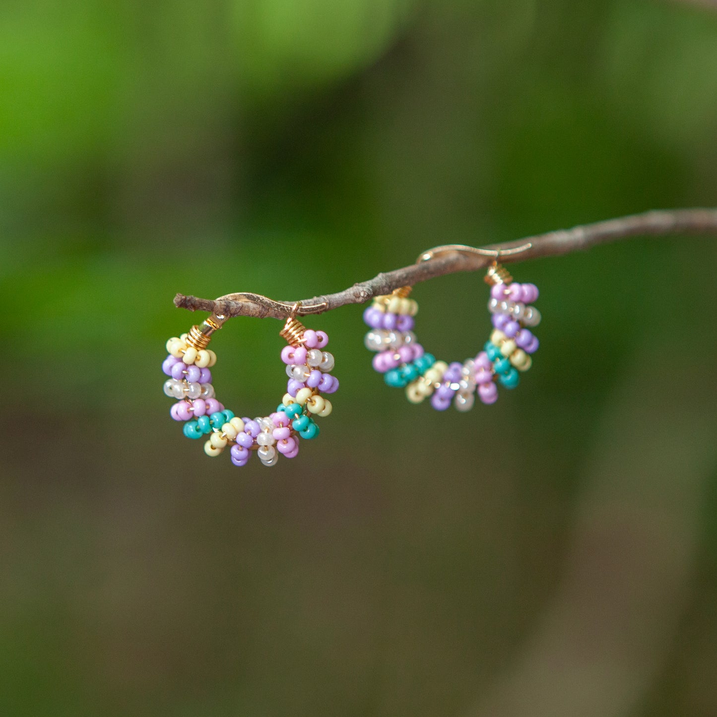 Handmade mini hoop earrings embellished with colorful beads and featuring bronze stud accents and gold plating.